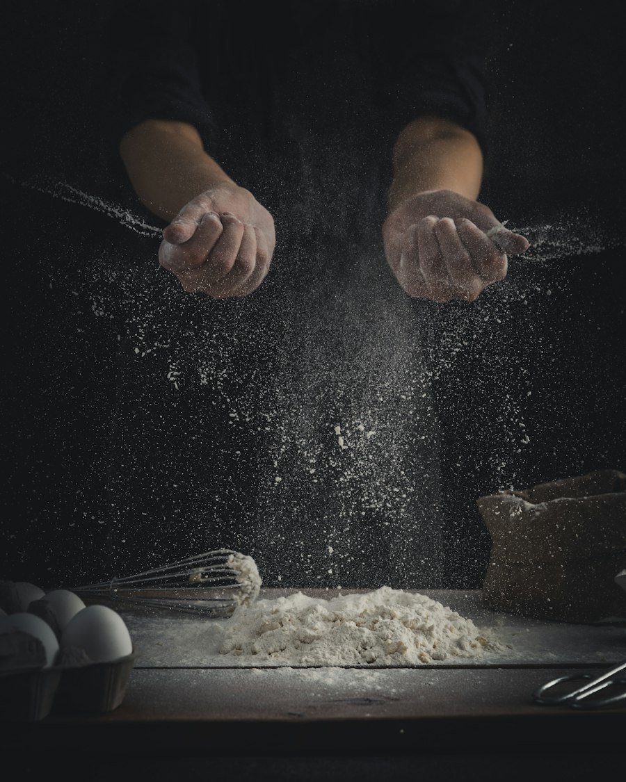 Flour being poured onto a table beside eggs and a whisk