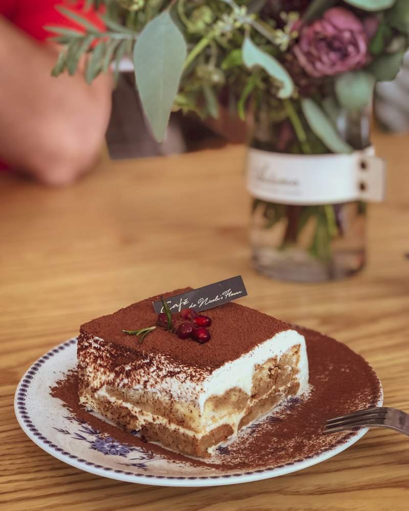 A slice of tiramisu on a plate, dusted with cocoa
