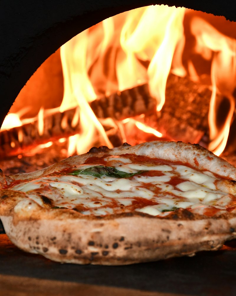 A pizza with melted cheese and tomato baking in a wood-fired oven
