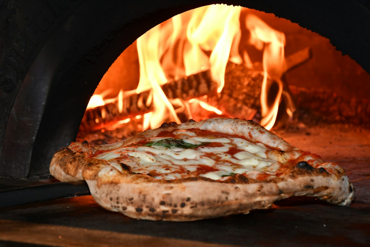 A pizza with bubbling cheese and tomato baking in a wood-fired oven