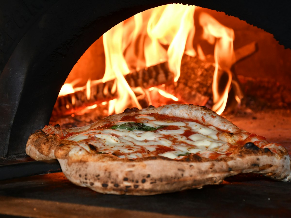 A pizza with melted cheese and tomato baking in a wood-fired oven