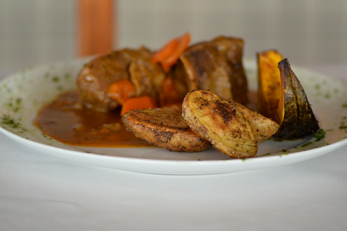 A white plate of cooked meat served with vegetables