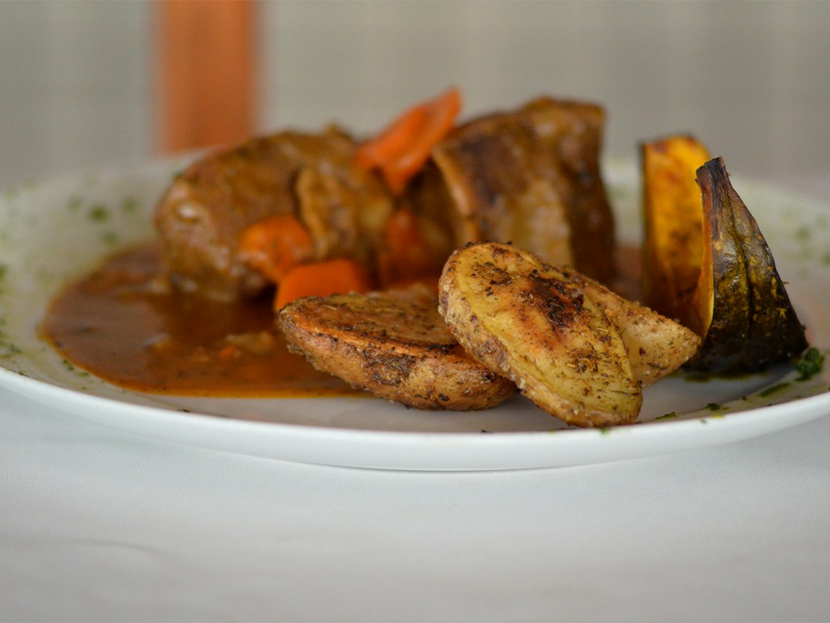 A white plate of cooked meat served with vegetables
