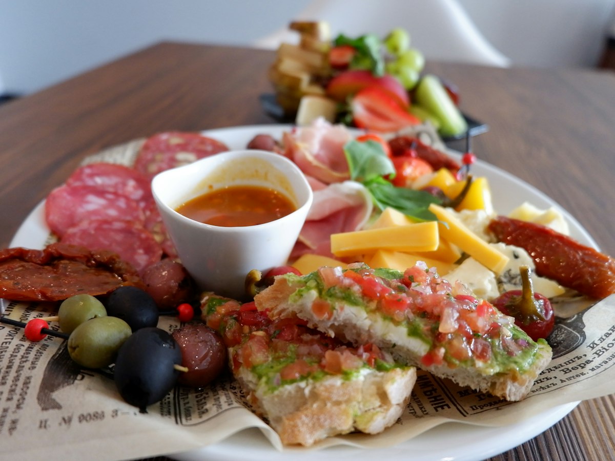 A wooden board of cured meats, cheese, olives and bread, laid out as antipasti