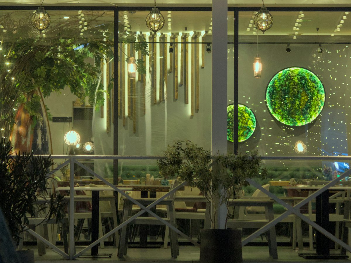 A restaurant glowing through its windows at night, with pendant lights and neatly set tables